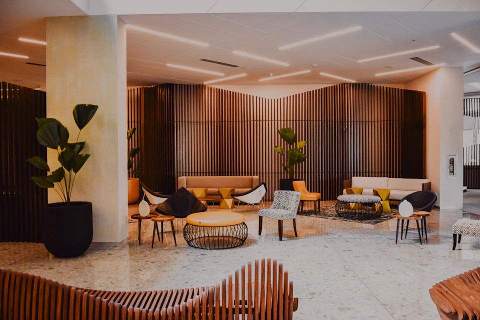 A warm, modern hotel lobby lounge with wooden slat walls, low sofas and plants