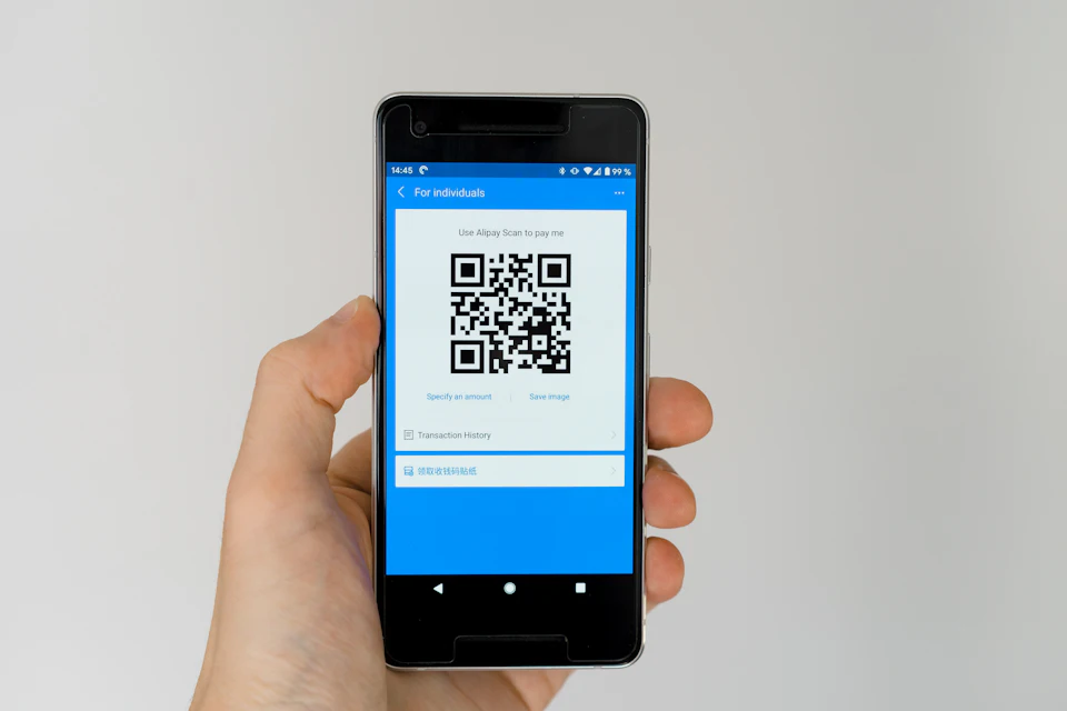 A hand holding a smartphone showing a QR code